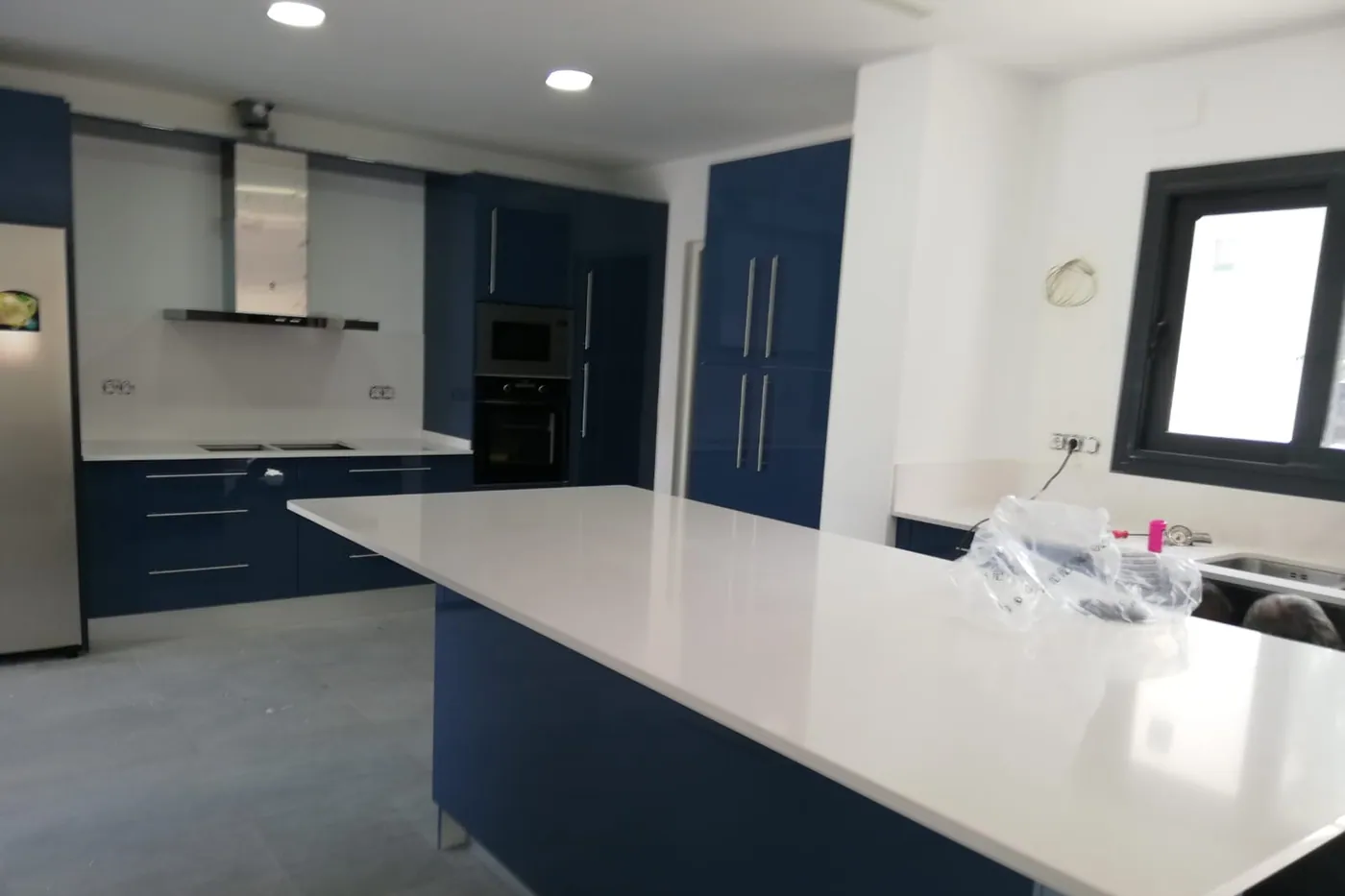 Cuina de front blau petroli amb illa central i encimera de superfície compacta blanca