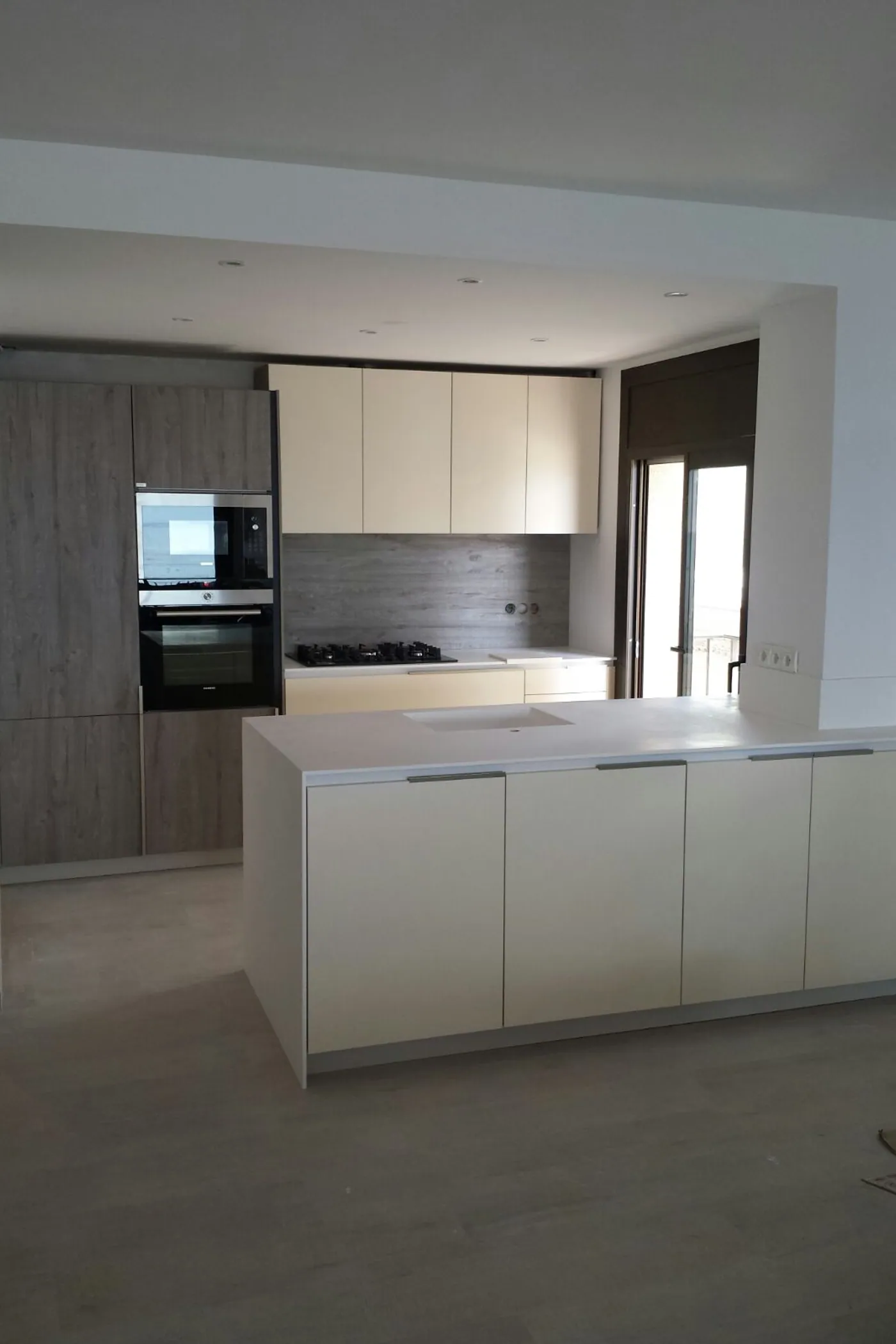 Cuina oberta amb illa central, columna de forn i microones i front blanc