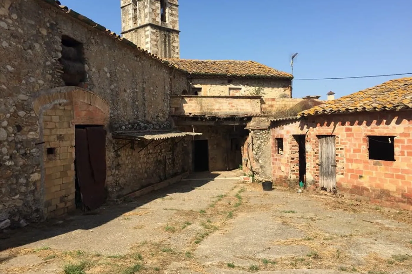 Pati de masia amb arc de maó i el campanar del poble al fons