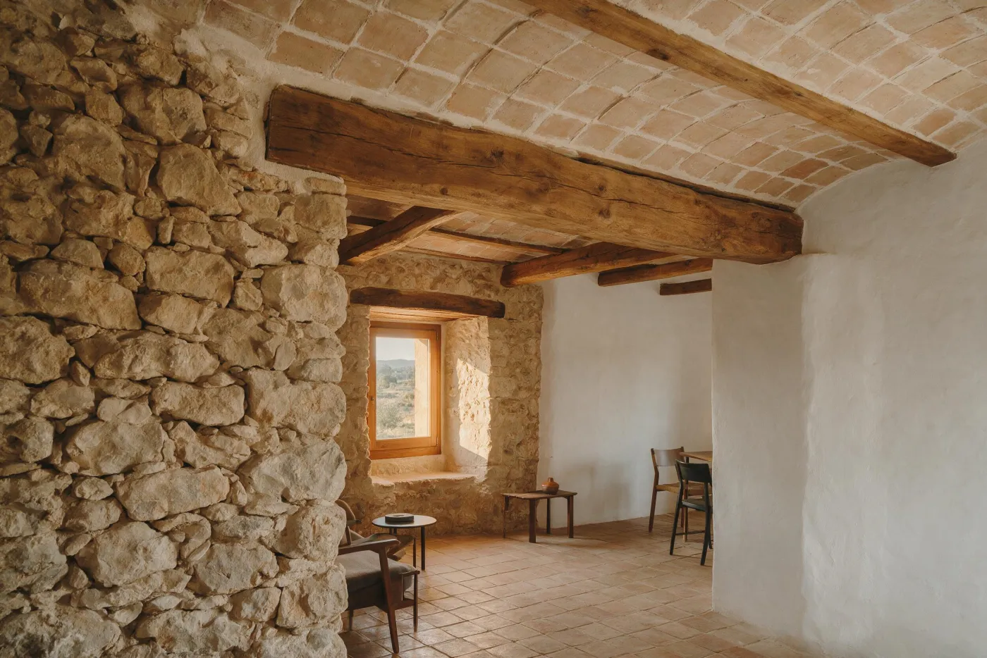Interior de masia rehabilitada amb parets de pedra vista, bigues de fusta i volta catalana